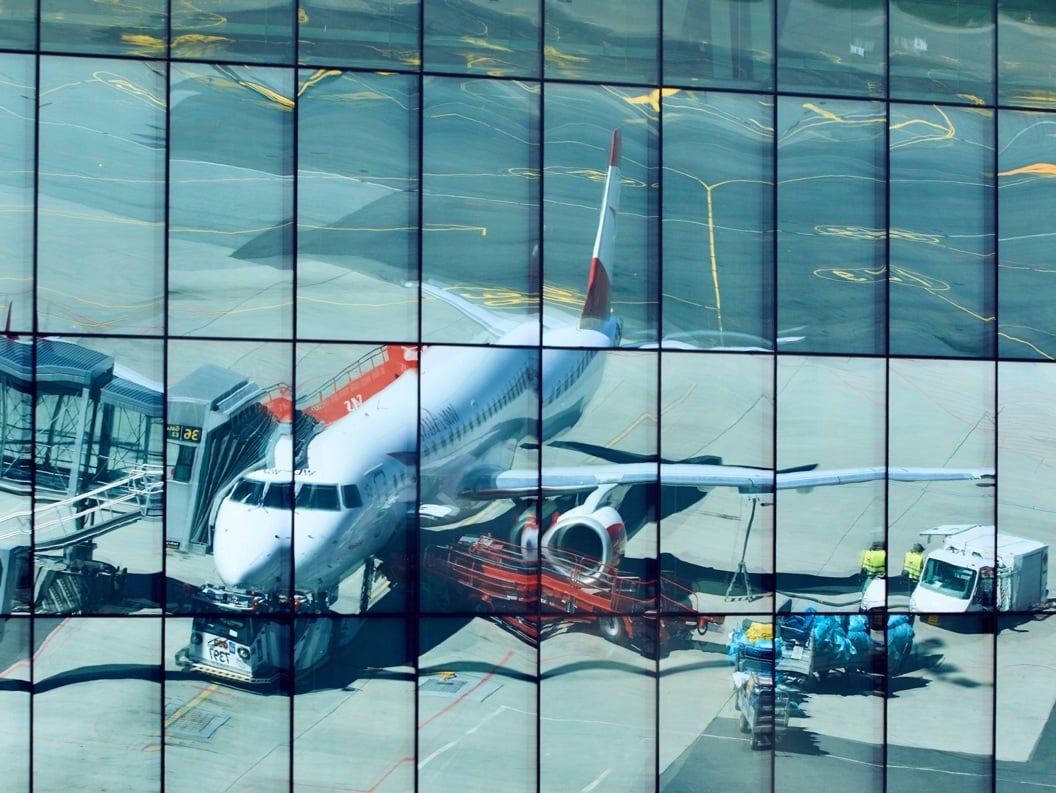 Refleksjon av et passasjerfly ved en flyplassgate, fanget på en glassfasade på en bygning