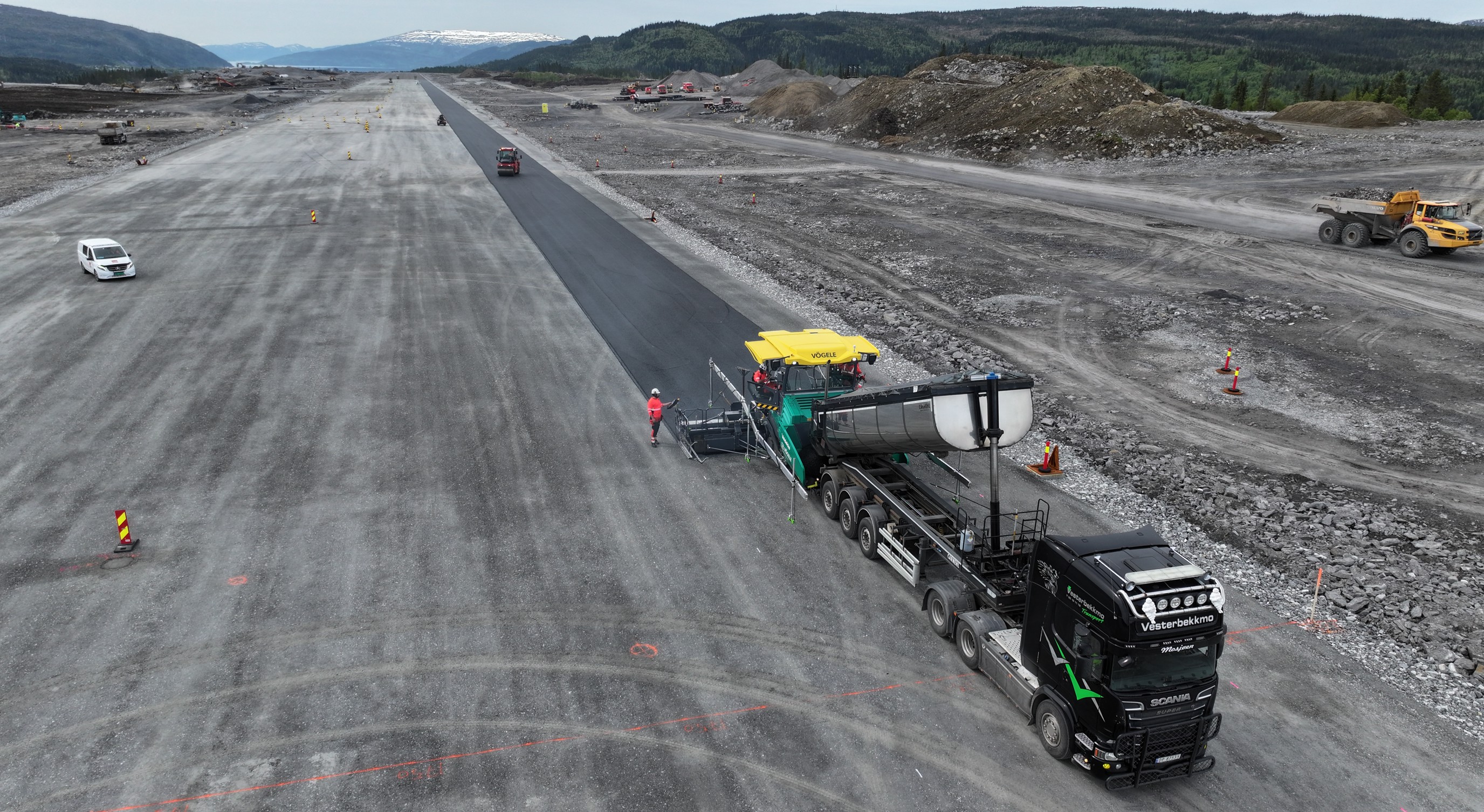 Asfaltlegging på flyplass i naturskjønne omgivelser med fjell i bakgrunnen