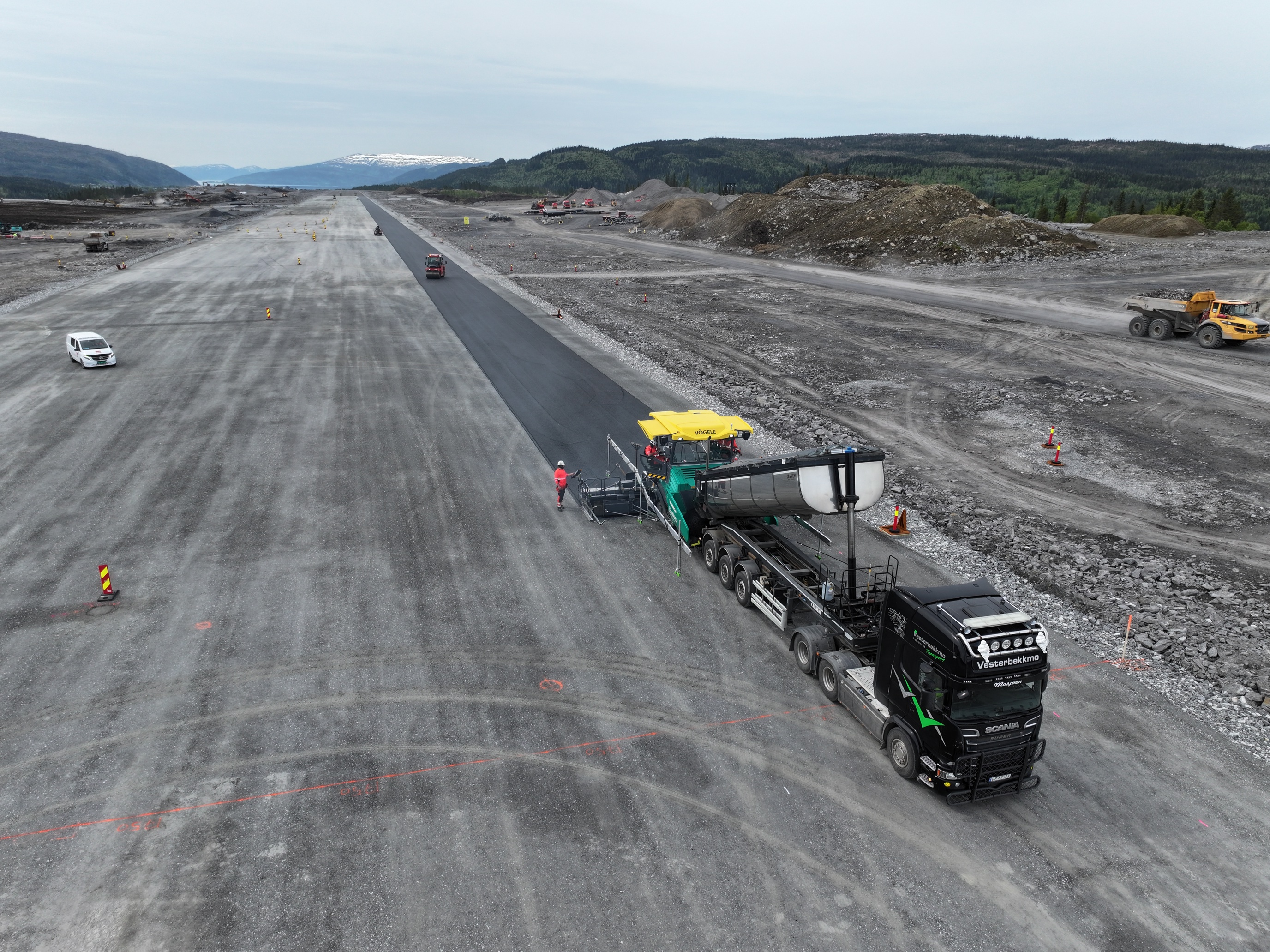 Asfaltlegging på flyplass i naturskjønne omgivelser med fjell i bakgrunnen