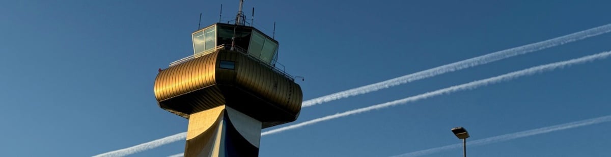 Flykontrolltårn på flyplass mot blå himmel med kondensstriper