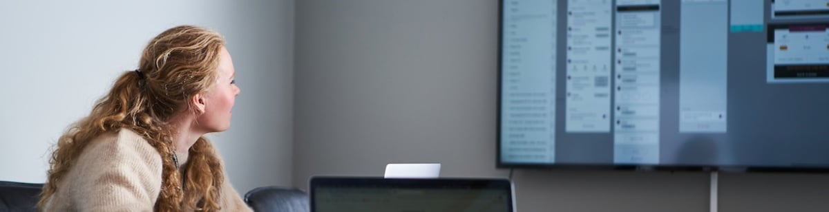 Kvinne på kontor ser på en stor skjerm med presentasjon eller digitalt innhold under et møte