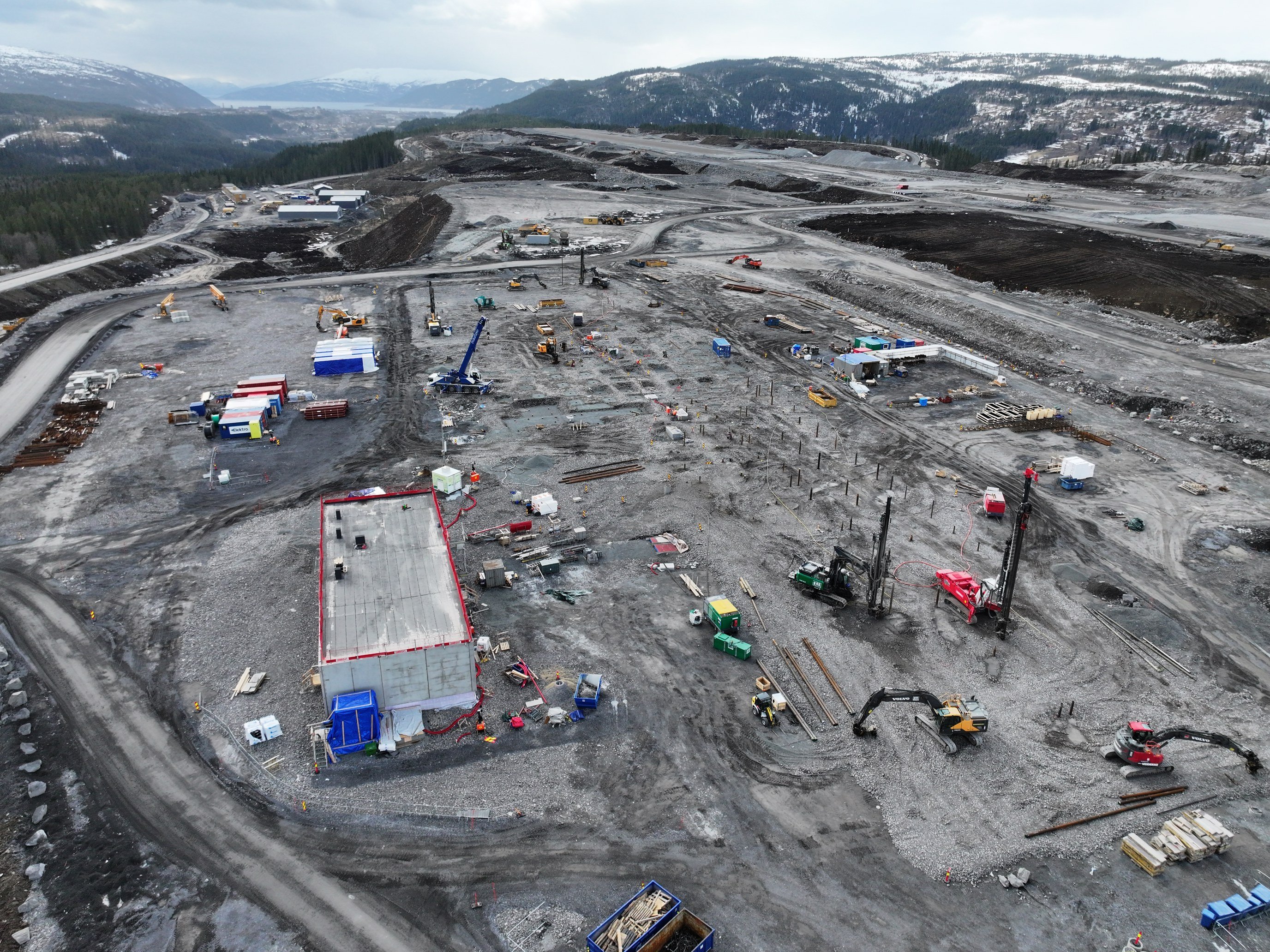 Byggeplass i naturskjønt fjellandskap med anleggsmaskiner og midlertidige containere, under utvikling