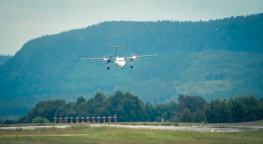 Lite passasjerfly på innflygning over en rullebane med fjell i bakgrunnen