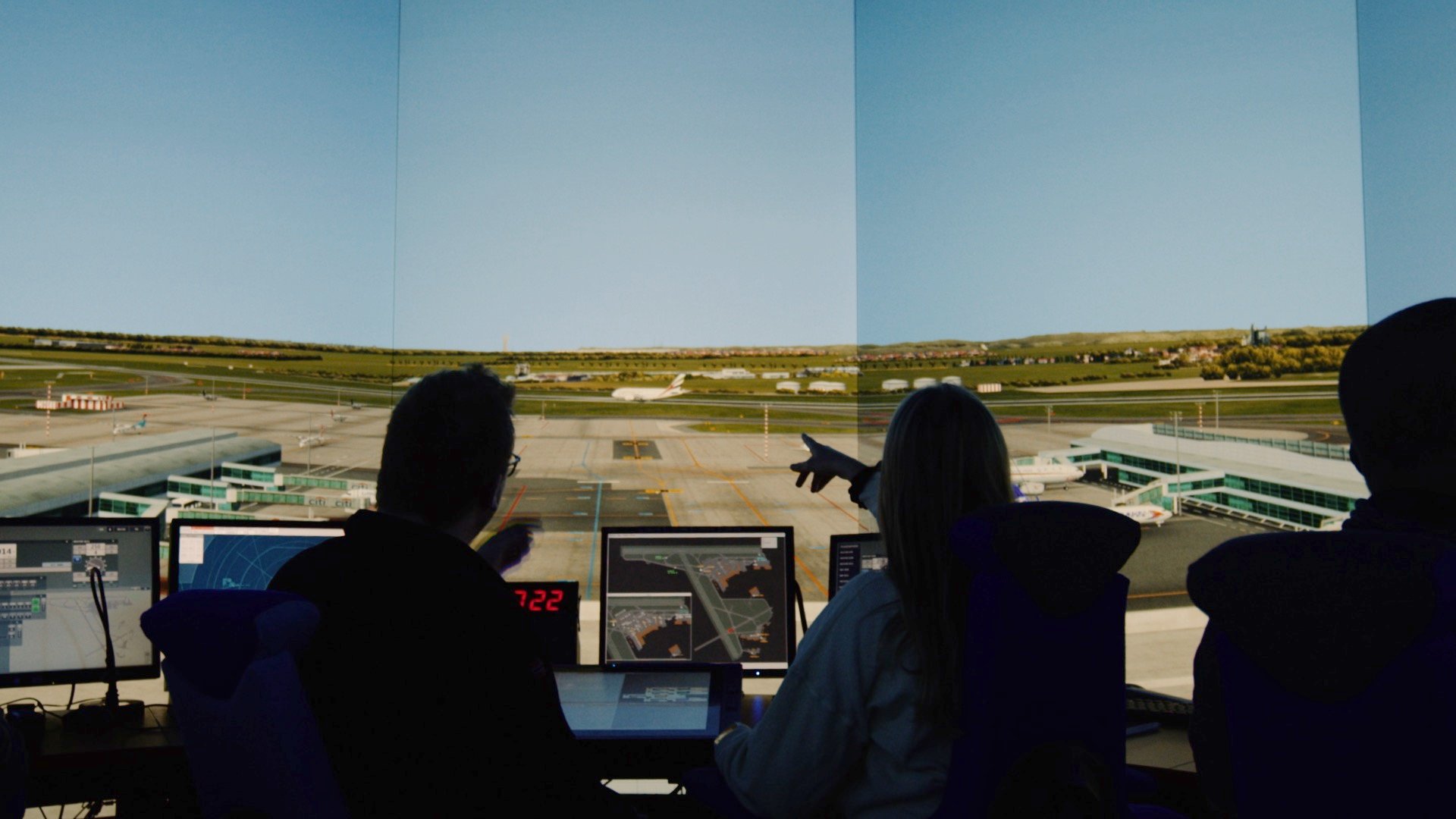 Kontrollrom på flyplass med personar som overvakar rullebanene frå skjermer