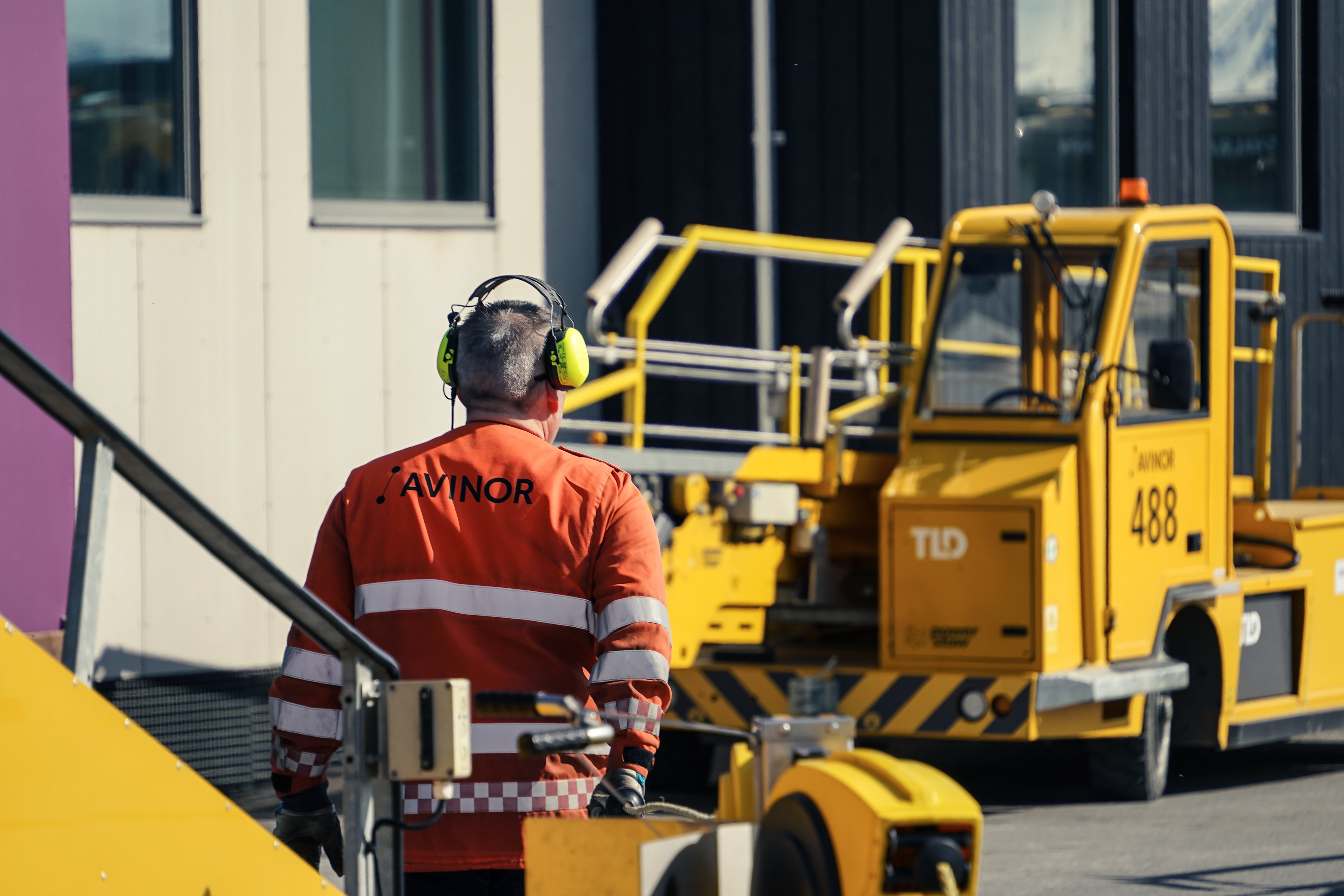 Ein flyplasstilsett med høyrselsvern går ved sidan av ein gul bakkehandteringstraktor på flyplassen