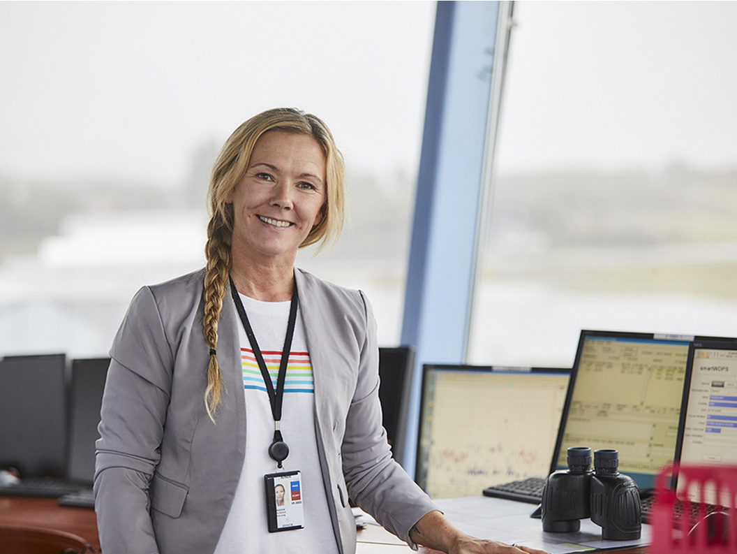 Smilende kvinne i et kontrollrom med dataskjermer og kikkert