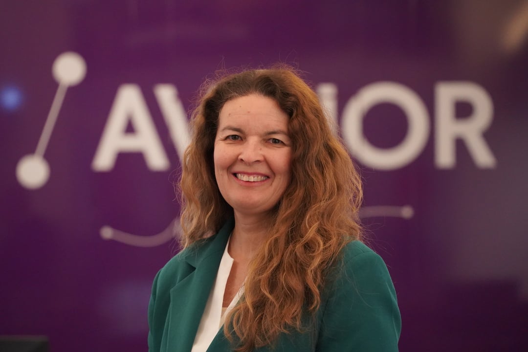 Kvinne i grønn jakke foran en lilla bakgrunn med teksten "AVINOR".