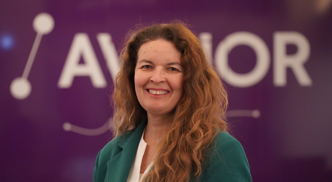 Kvinne i grøn jakke framfor ein lilla bakgrunn med teksten "AVINOR".