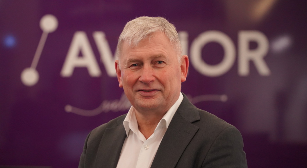 Mann med grått hår smiler foran ein liten bakgrunn med teksten "AVINOR".