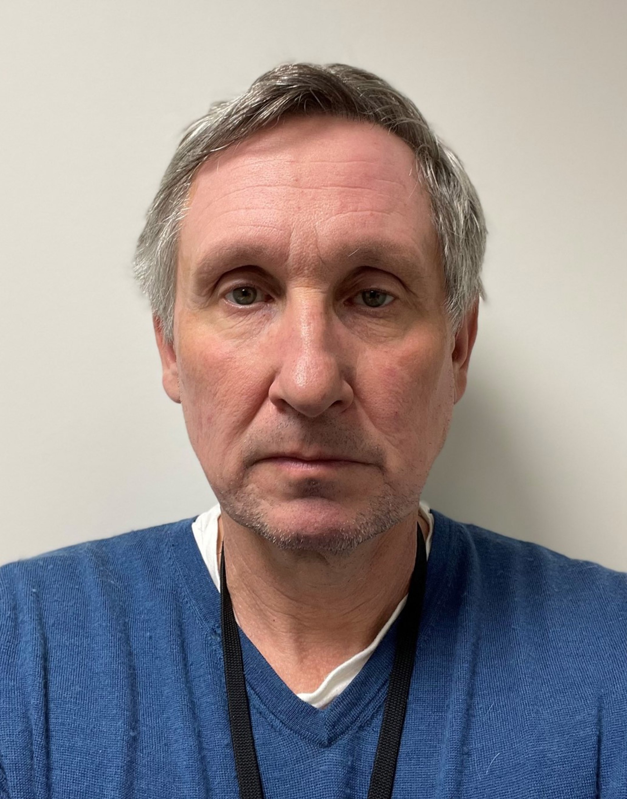 Portrett av ein mann med grått hår iført ein blå genser, ser direkte inn i kameraet. Bakgrunnen er nøytral og lysegrå