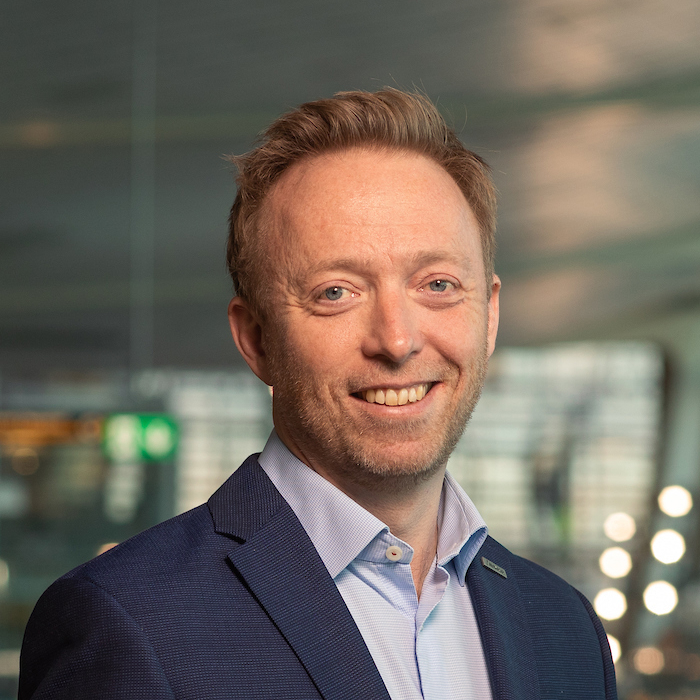 Forretningsmann i blå dress smiler i moderne kontormiljø.