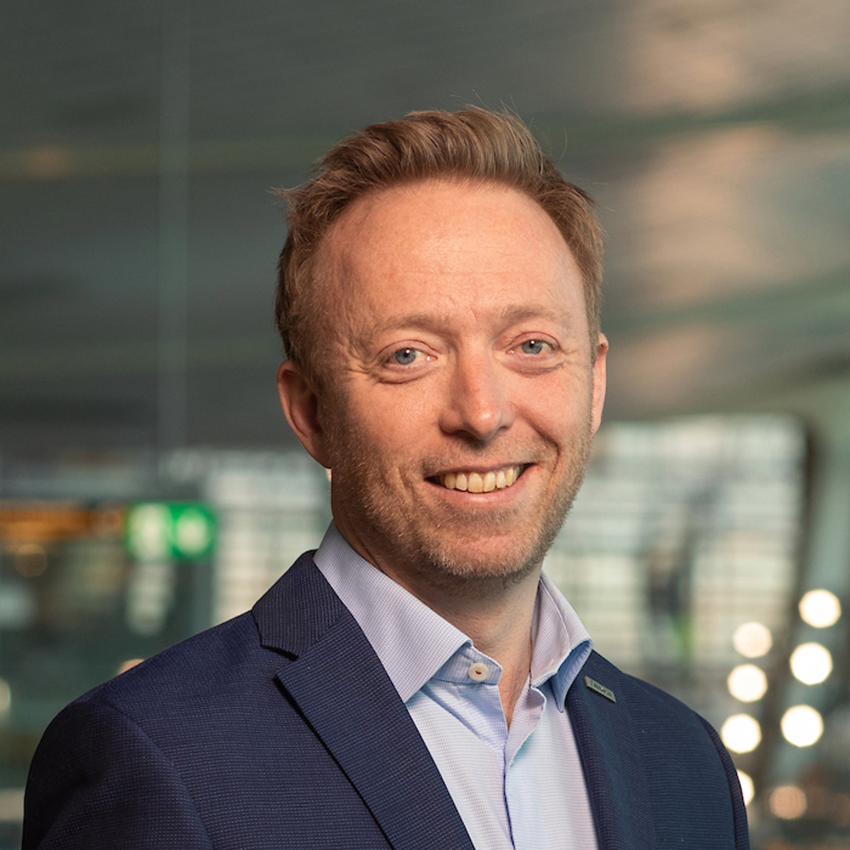 Forretningsmann i blå dress smiler i moderne kontoromgivelse.