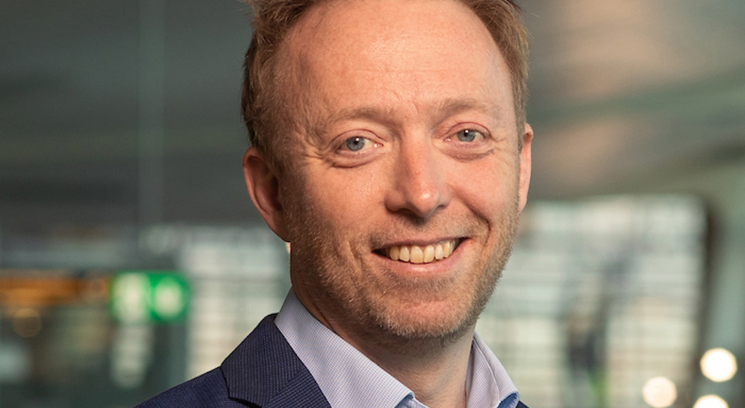 Forretningsmann i blå dress smiler i moderne kontormiljø.