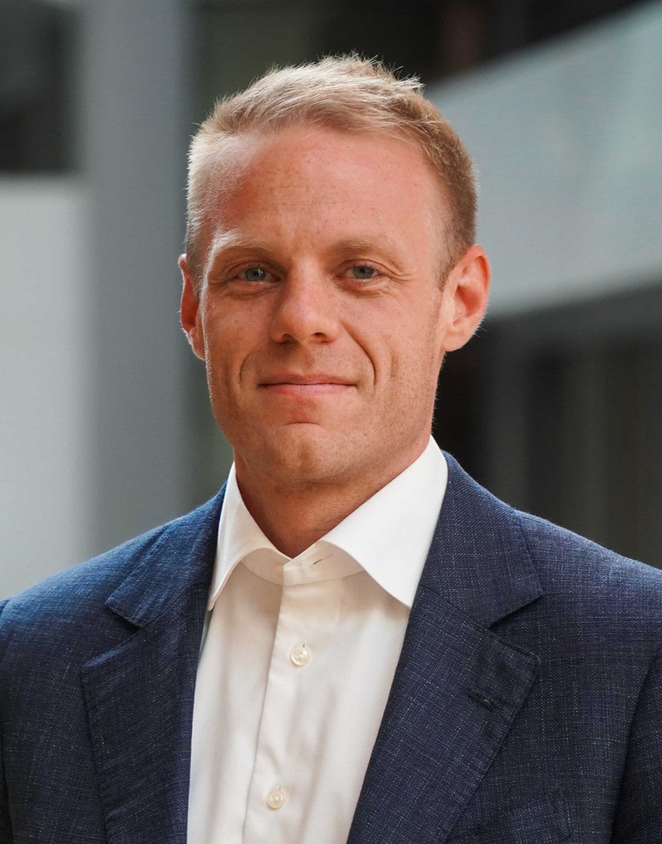 Mann iført dressjakke og kvit skjorte, står i eit kontormiljø