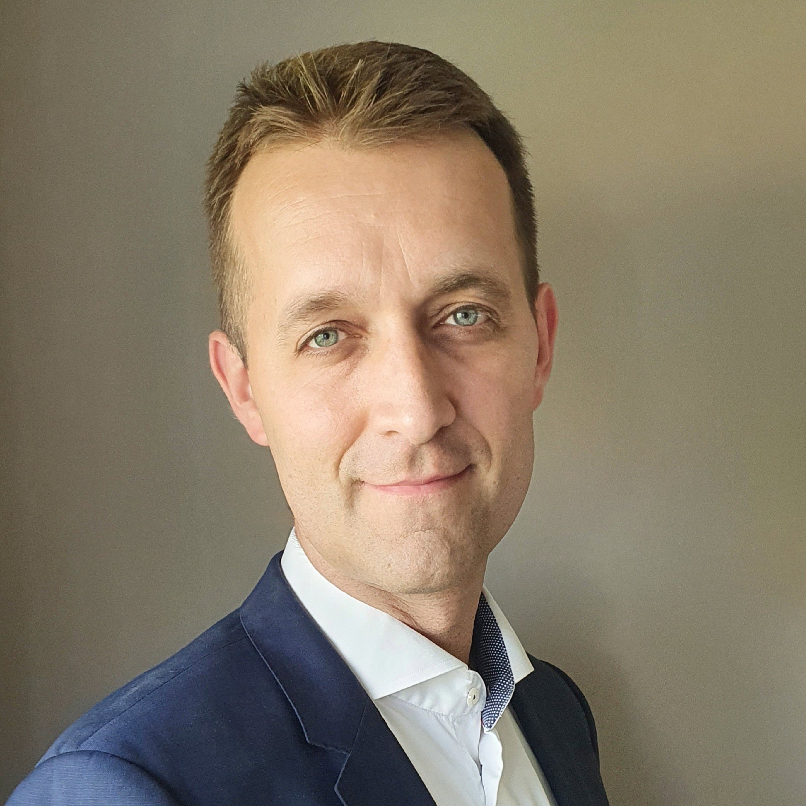 Mann i dressjakke smiler mot kameraet, med nøytral bakgrunn.