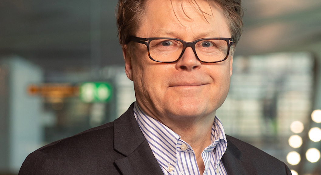 Person i dressjakke og briller i moderne kontorinteriør.