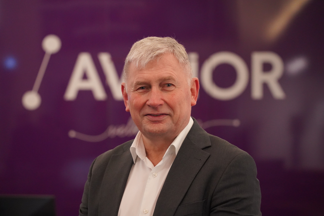 Mann med grått hår smiler foran ein liten bakgrunn med teksten "AVINOR".