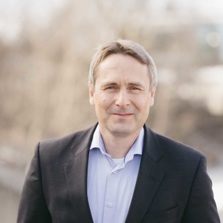 Mann med grått hår smiler foran en liten bakgrunn med teksten "AVINOR".
