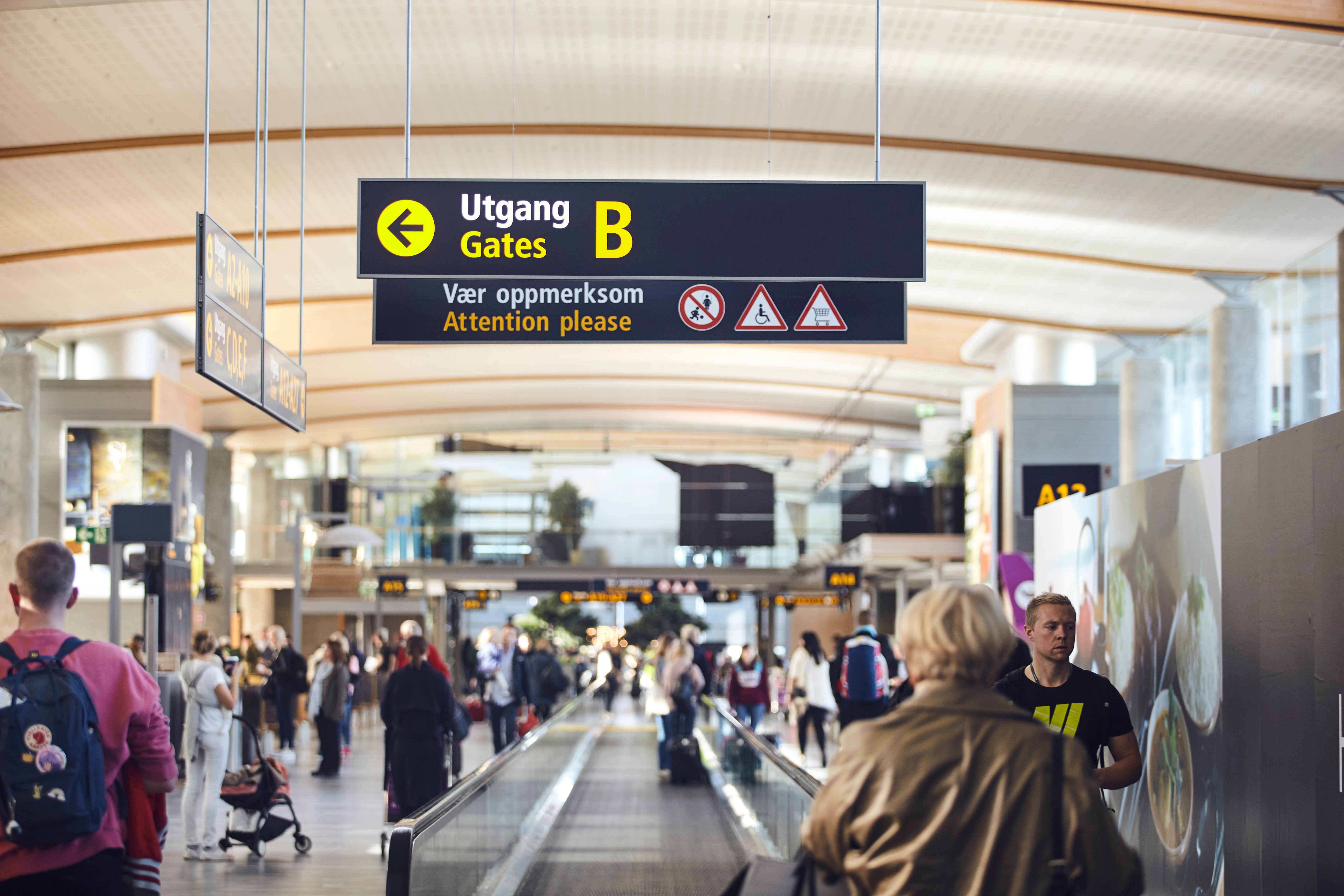People at the airport are moving toward exit B, with signs showing the way and giving warnings about smoking, mobile phone use, and wheelchair access.