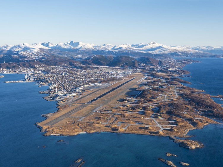 Flyfoto av Bodø by i Noreg, med flyplass og fjell i bakgrunnen på ein solfylt dag.