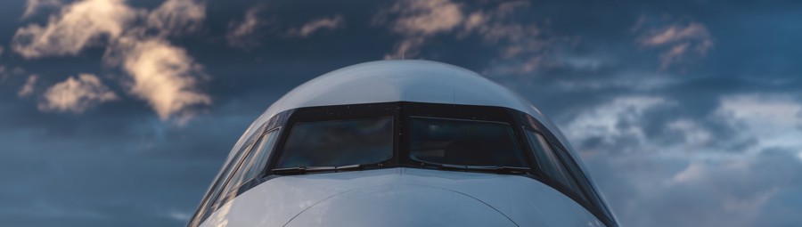 Nærbilde av cockpiten til et kommersielt passasjerfly mot en dramatisk kveldshimmel