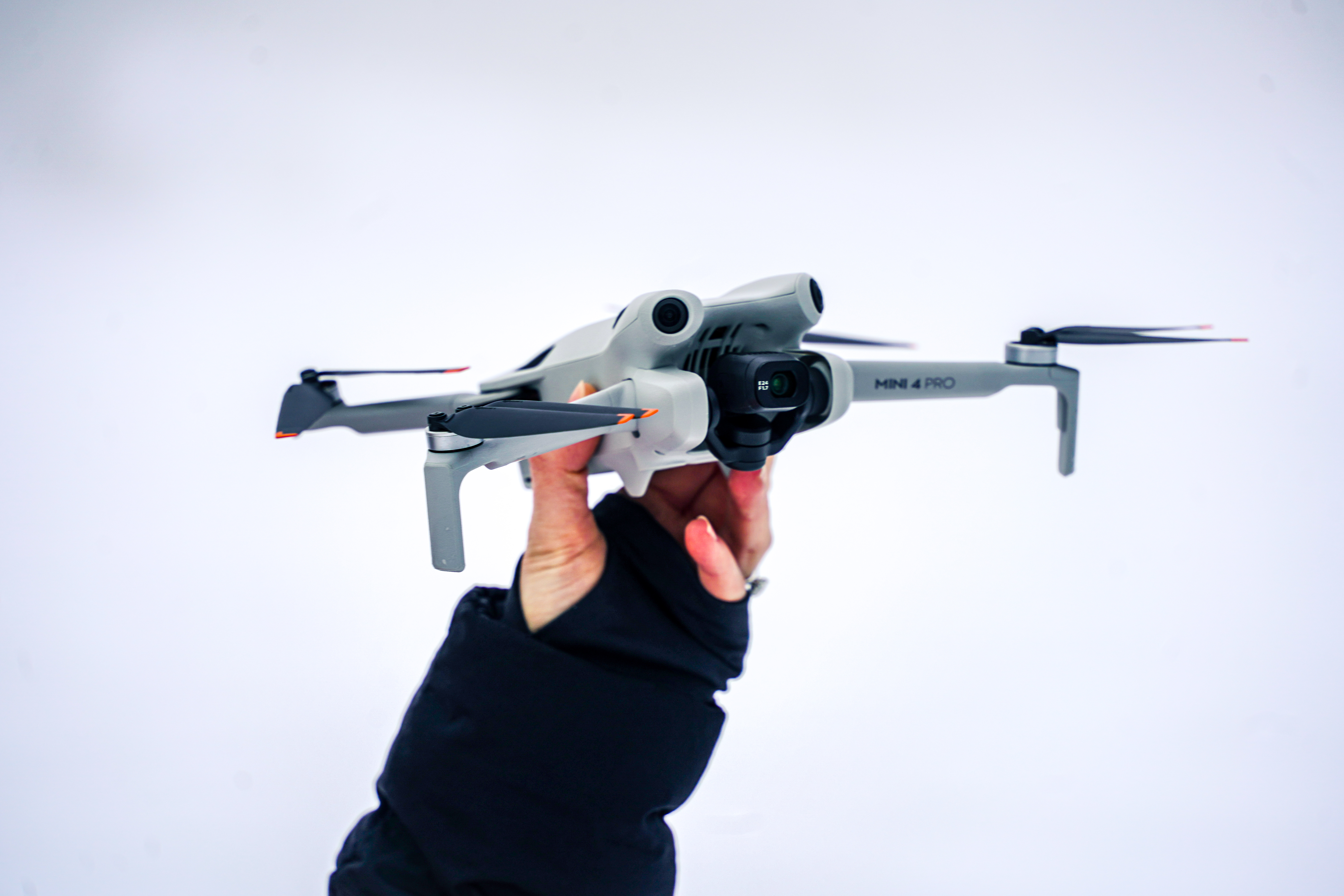 Hånd som holder en grå drone med fire propeller mot en hvit bakgrunn.