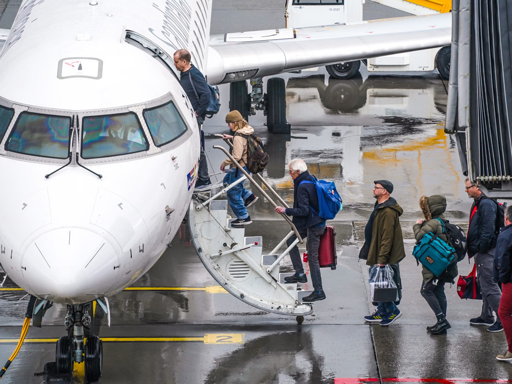 Passasjerar går om bord i eit fly på ein regntung dag på flyplassen.