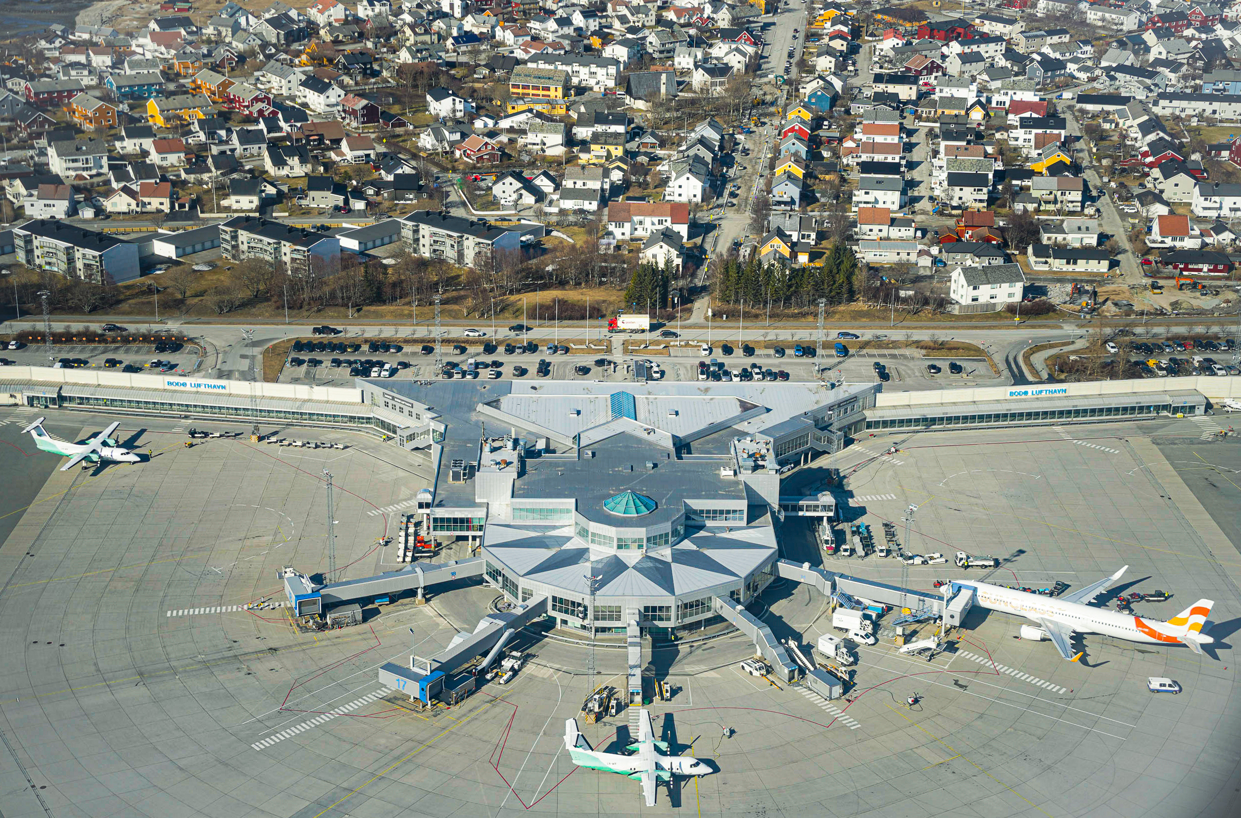 Aerial photo of Bodø Airport with planes on the ground, terminal building, and surrounding neighborhoods in Bodø, Norway.