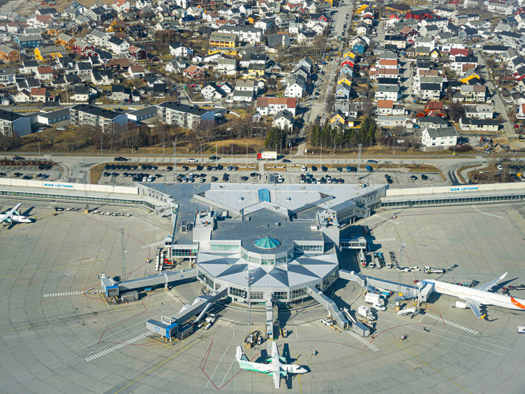 Flyfoto av Bodø lufthamn med fly på bakken, terminalbygning og omkringliggjande nabolag i Bodø, Noreg.