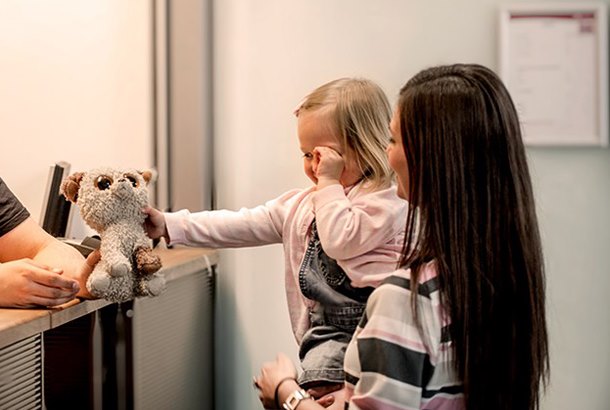 Småbarn og kvinne ved resepsjon, barnet holder en kosedyr