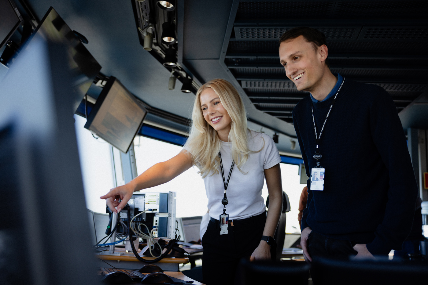 Two people in a control room looking at a screen, smiling and engaged in their work.