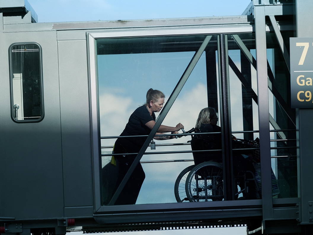 Flyplassansatte hjelper en passasjer i rullestol på en bro nær Gate 77