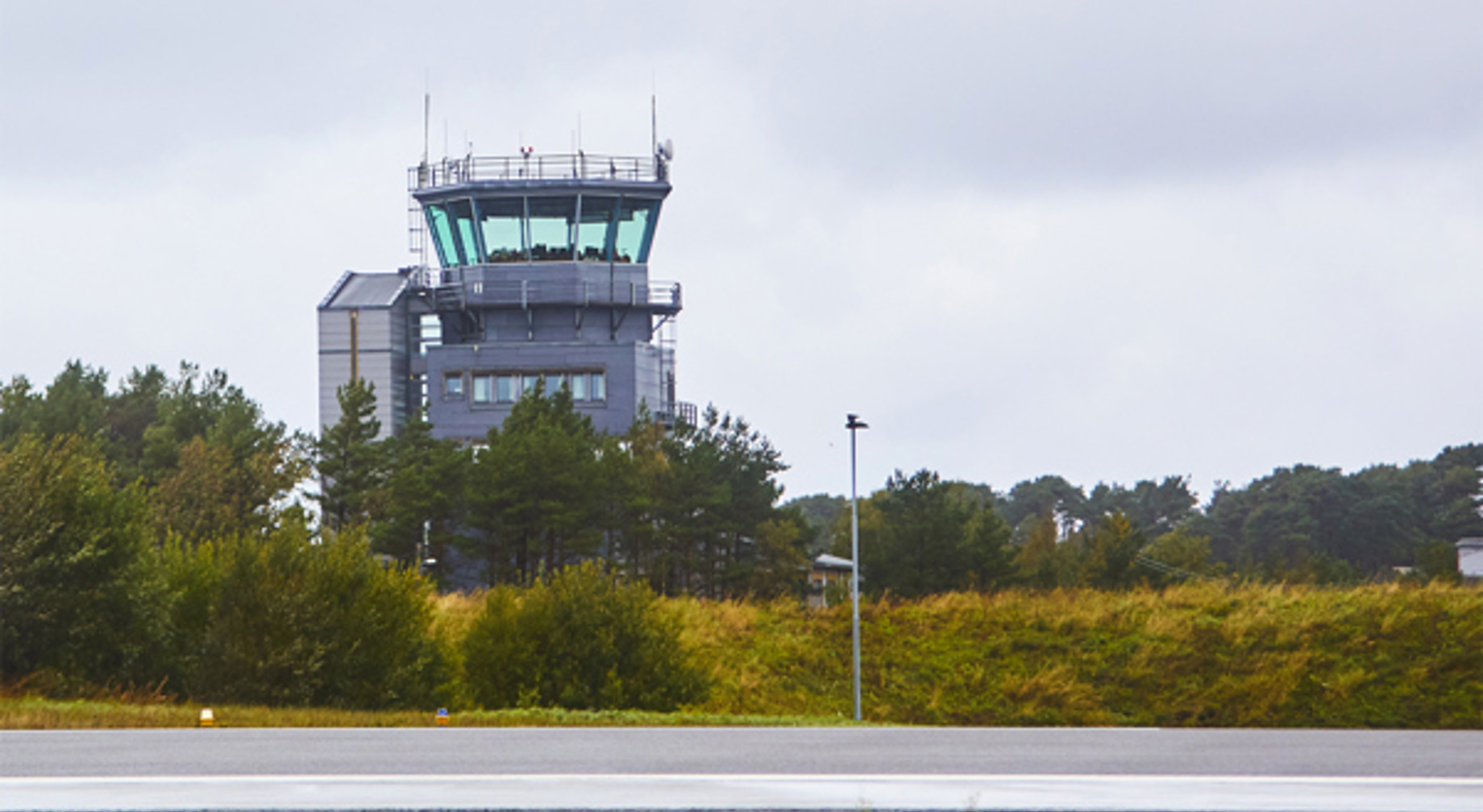 Airport terminal next to a runway on an overcast day, surrounded by trees and vegetation