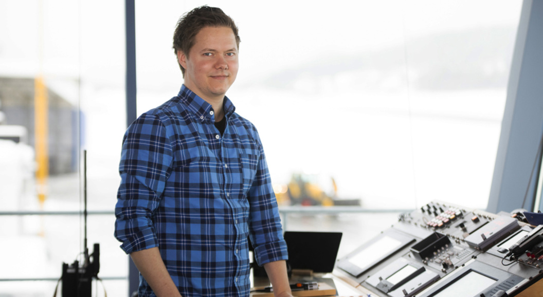 A person in a blue plaid shirt stands at a control desk with screens and equipment, overlooking a snowy background.