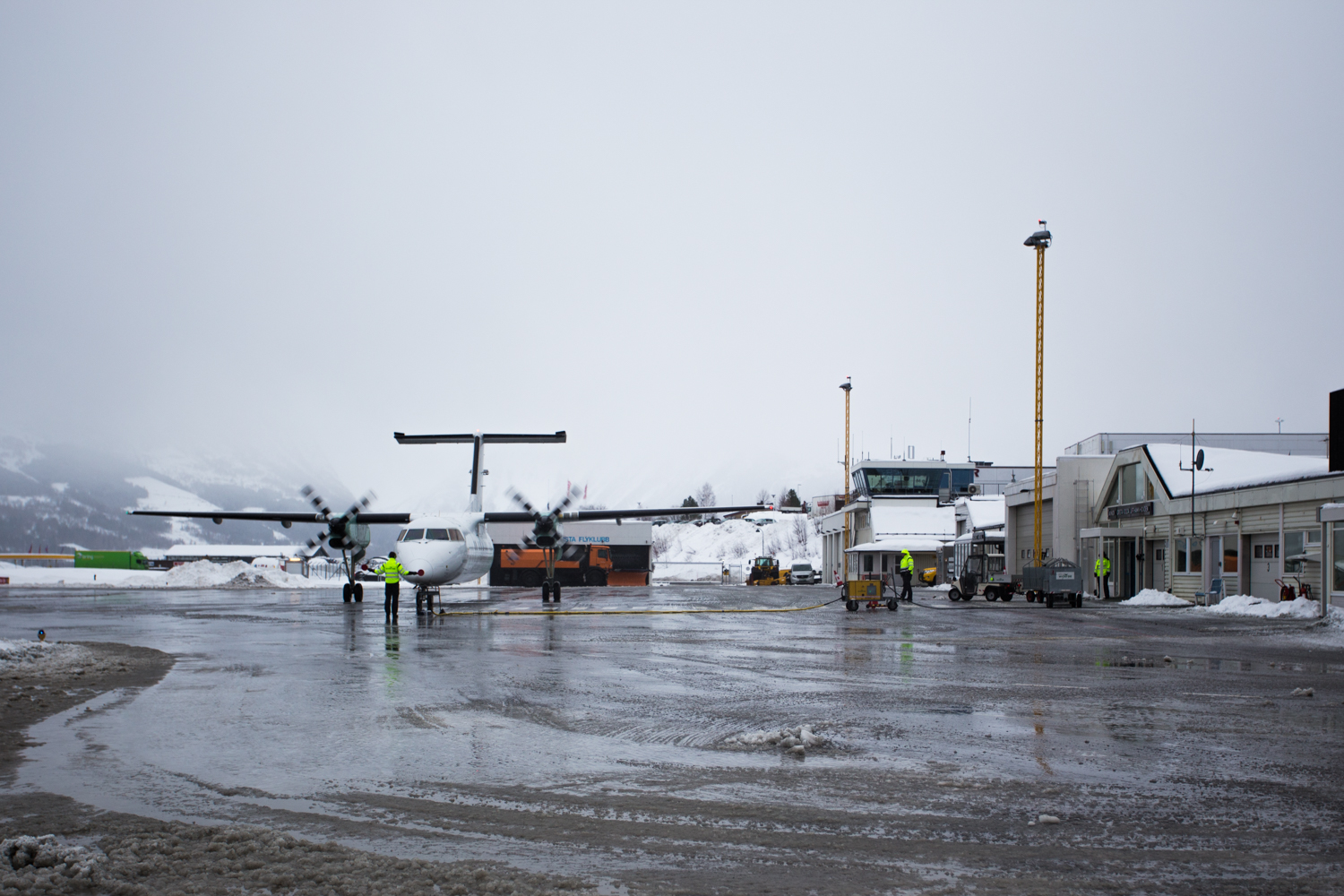 Airport with planes on the runway in winter, surrounded by snow-covered mountains.
