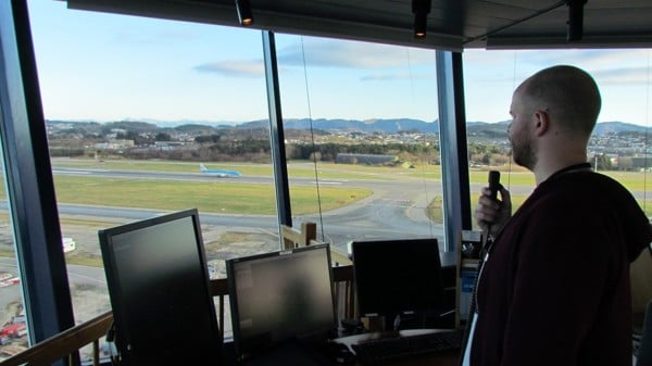 Air traffic controller in the control tower monitors airport air traffic, with a view of the runway and the landscape in the background.