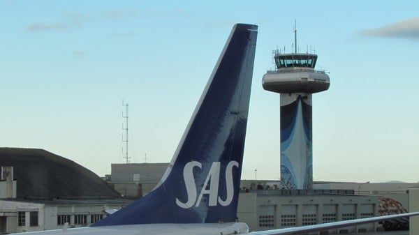 Airplane with SAS logo in front of an airport with a control tower in the background. Clear sky and modern infrastructure.