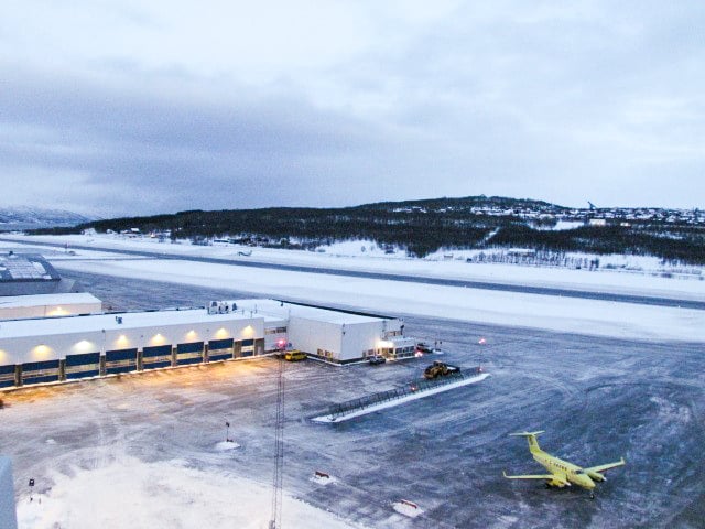 Airport with snow-covered runway at dawn, yellow plane parked next to hangar.
