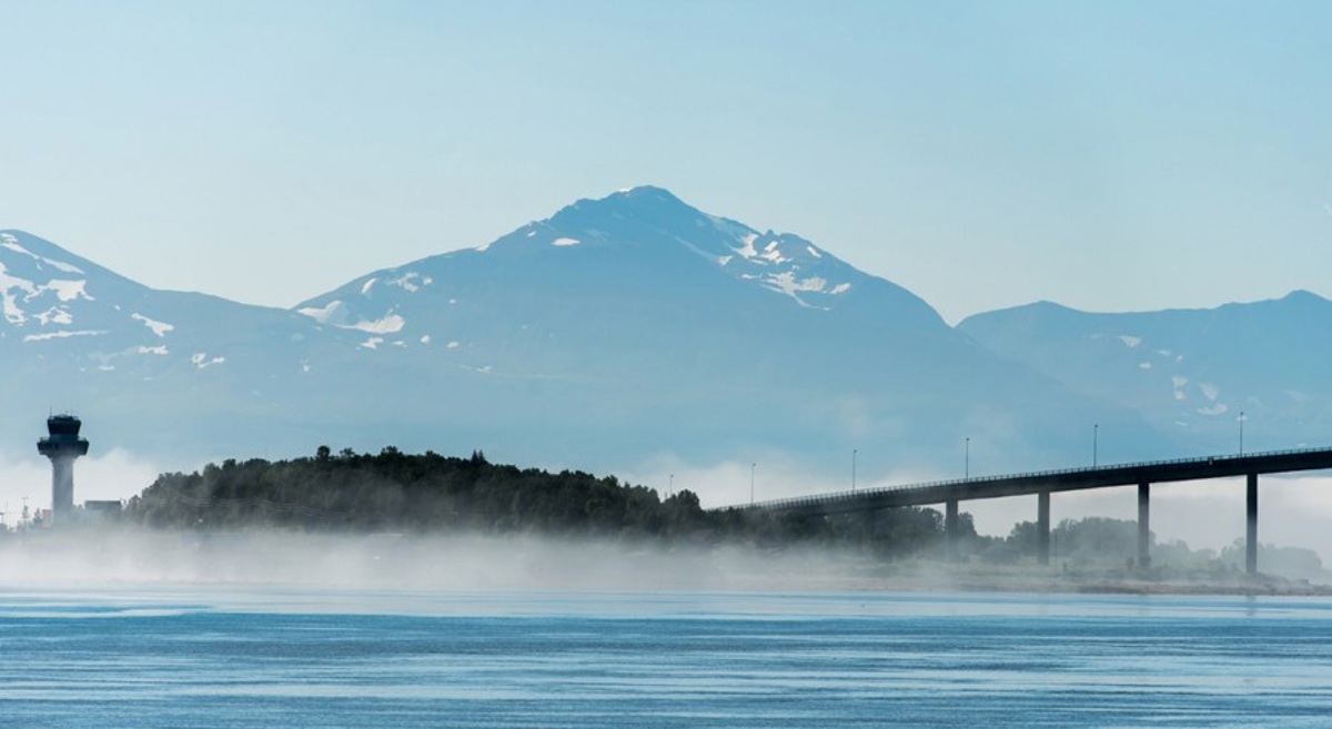 Bro over vann med fjell i bakgrunnen ved Ålesund, Norge, innhyllet i tåke.