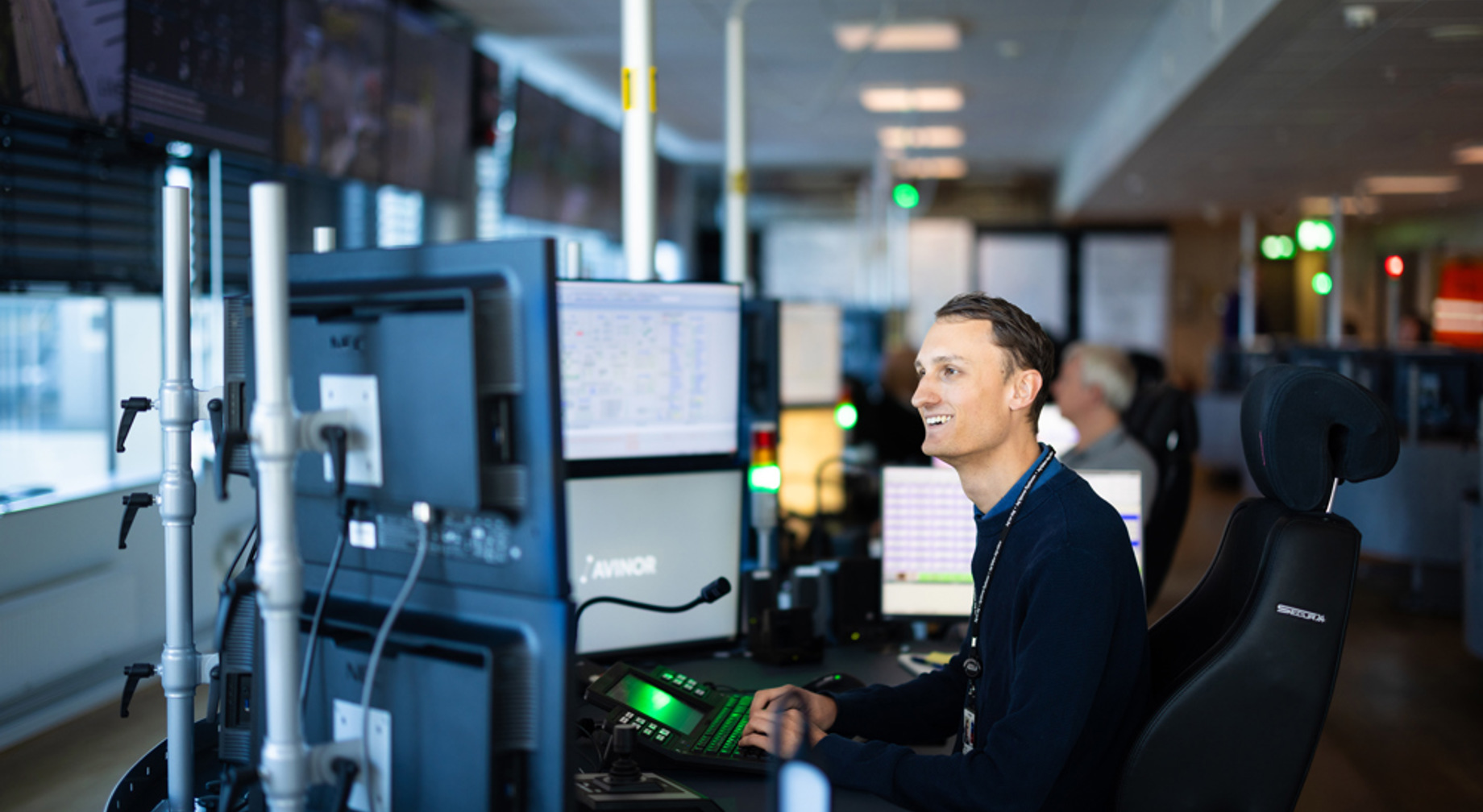 Kontrolltårn på flyplass med flygeledere i samtale, skjermer i bakgrunnen.