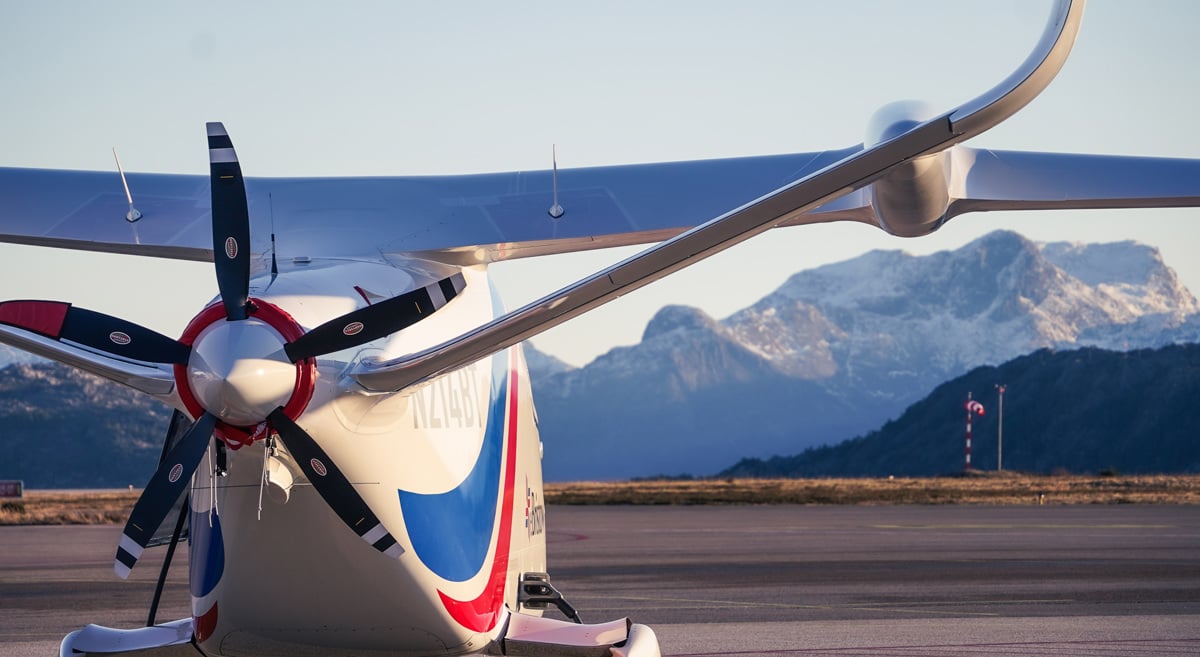 Elektrisk fly ved flyplass med fjell i bakgrunnen under en klar himmel.