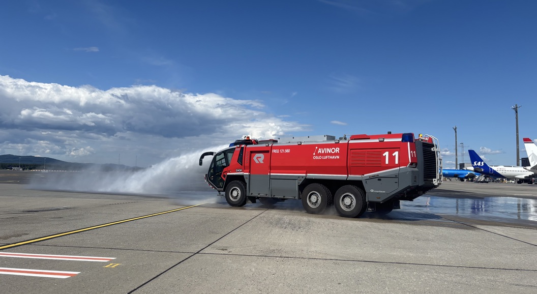 Brannbil fra Avinor Oslo Lufthavn som sprøyter vann på flyplassrullebanen, med SAS-fly i bakgrunnen