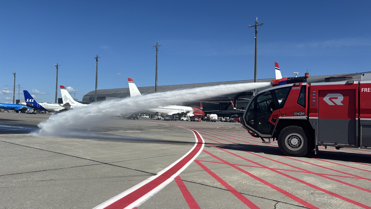 Brannbil på flyplass sprøyter vann over rullebanen foran passasjerfly og SAS-fly ved terminalen