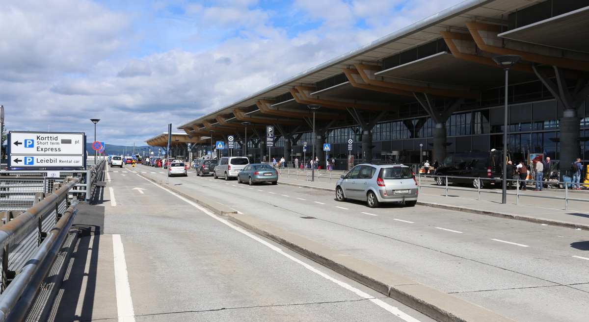Utenfor en Oslo lufthavns flyplassterminal med biler, parkeringsskilt og reisende ved avgangs- og hentesone