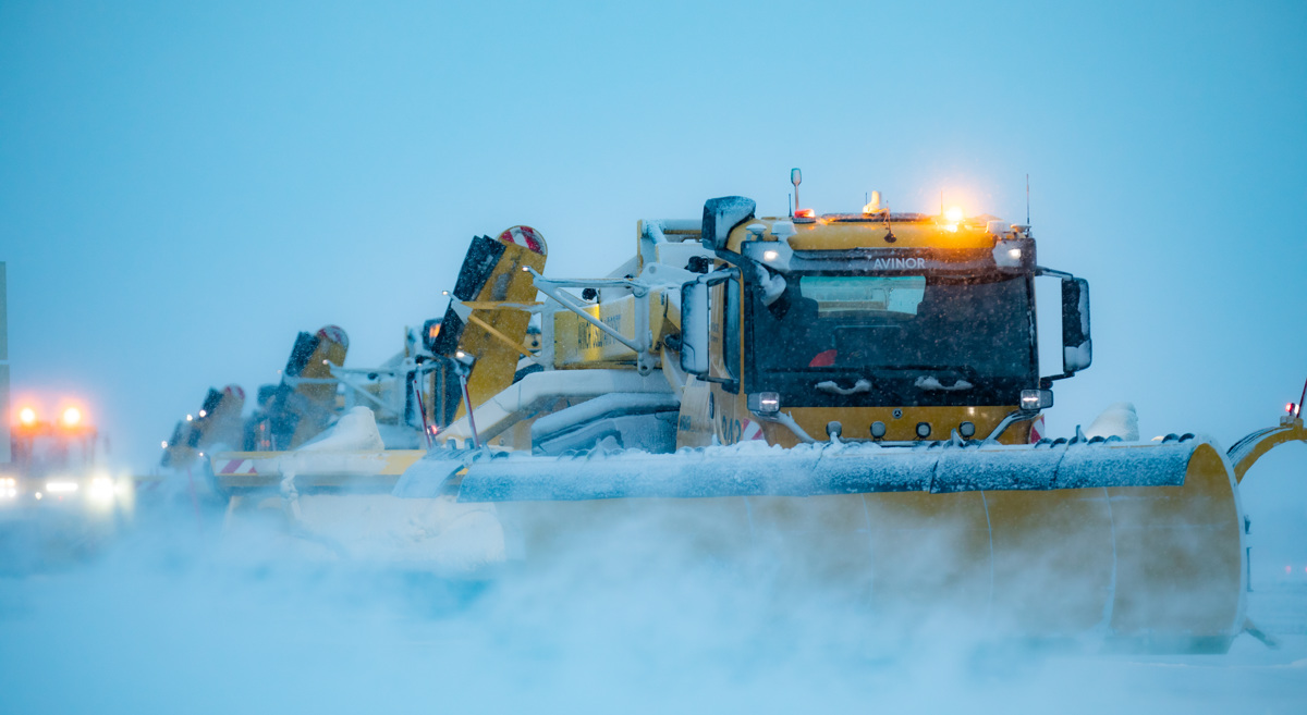 Snøploger rydder flyplassbanen i kraftig snøvær, med lysene på for å sikre sikker operasjon