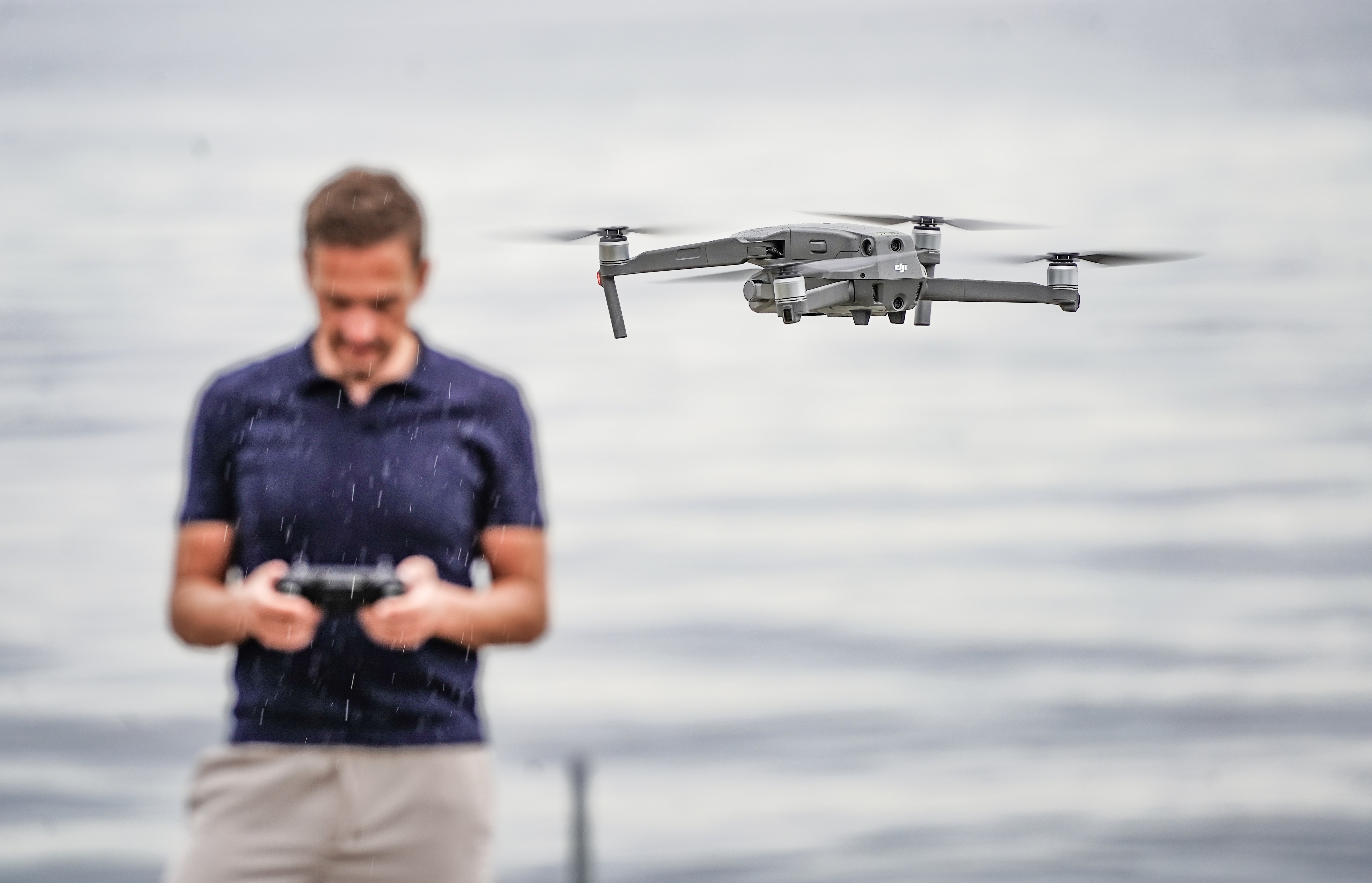 Ein mann kontrollerer ein flygande drone ved ein innsjø