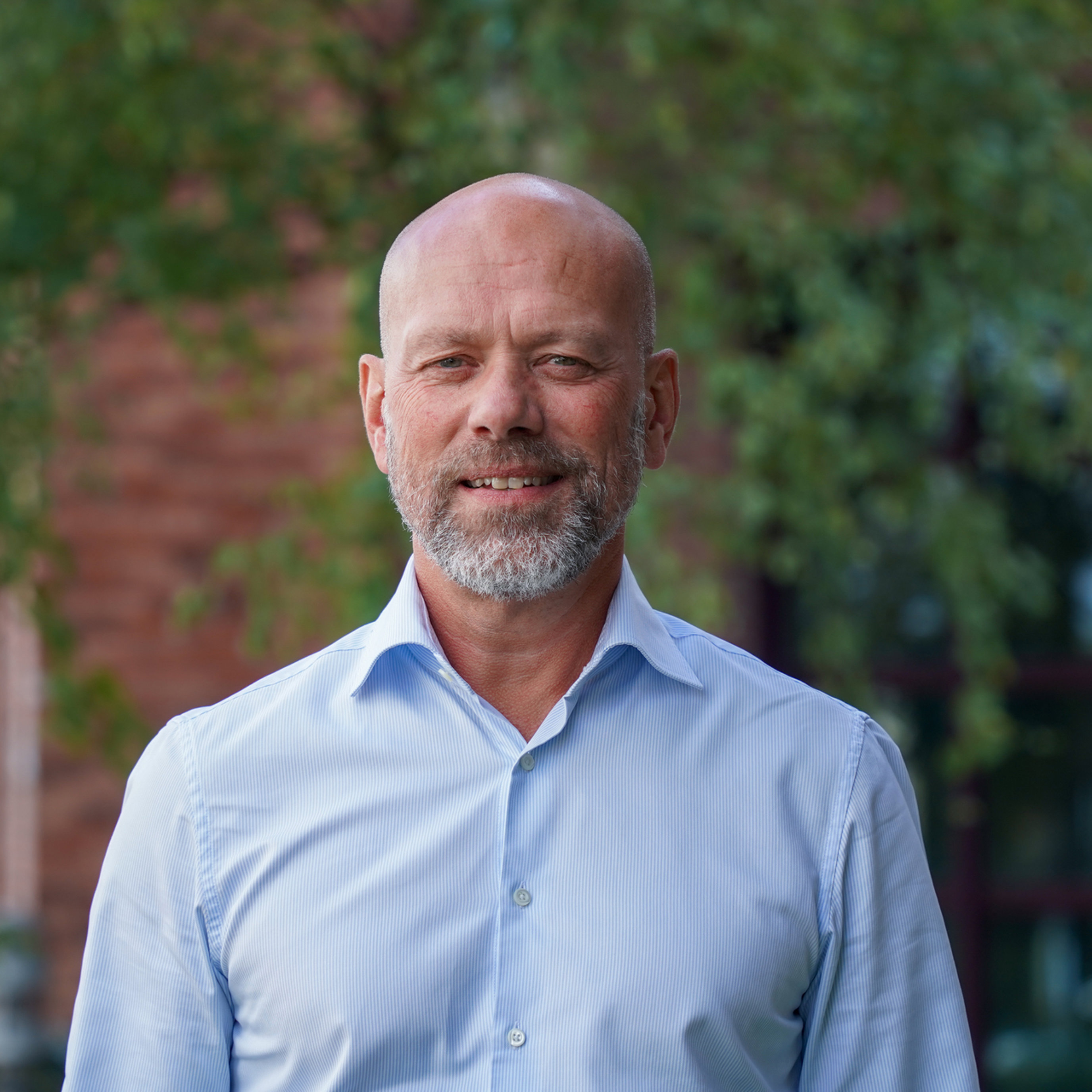 Ein smilande mann med skjegg og blå skjorte står ute framfor ein grøn bakgrunn.