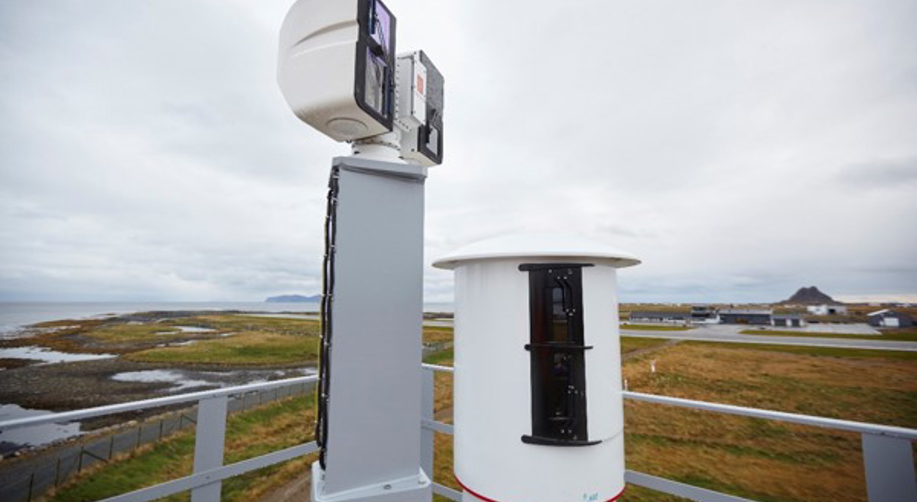 To radarantenner på ein utendørs plattform med norsk kystlandskap i bakgrunnen