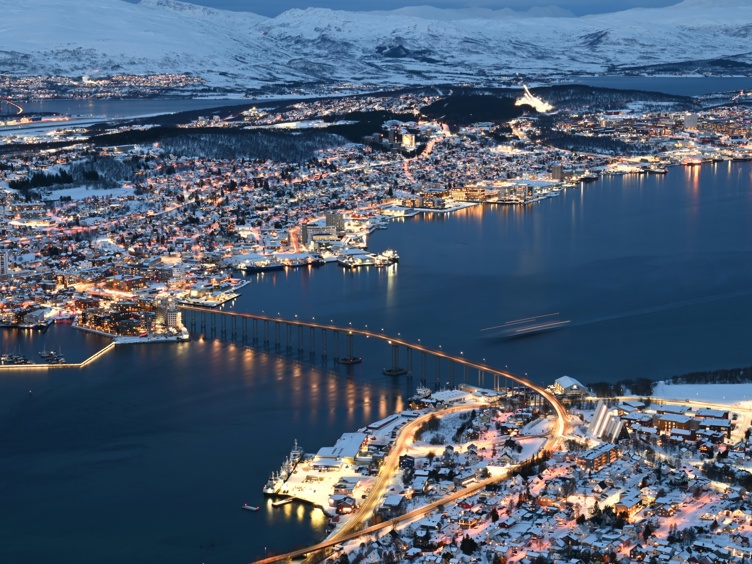 Flyfoto av Bodø by i Norge, med flyplass og fjell i bakgrunnen på en solfylt dag.