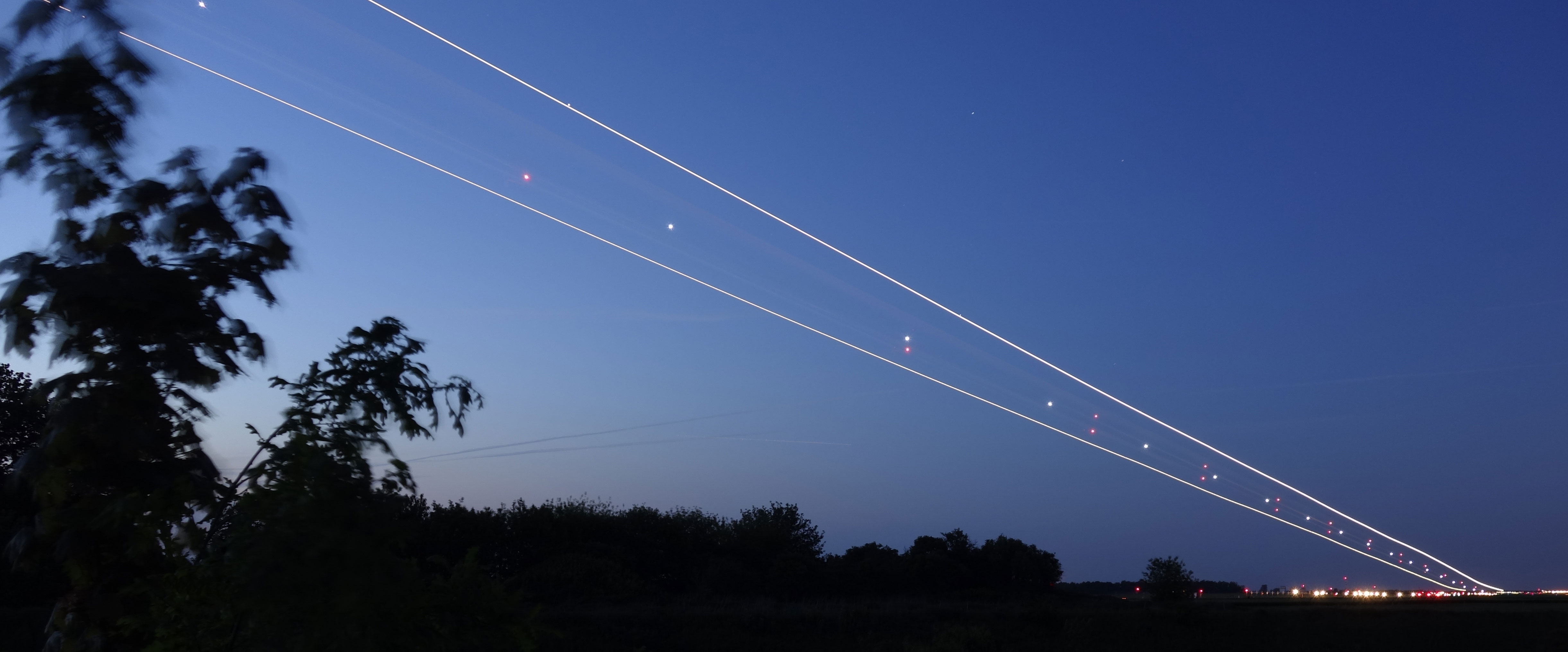 Lang eksponering av stjerneklar himmel med flylys i bevegelse over natthimmel, omgitt av skogkledd horisont